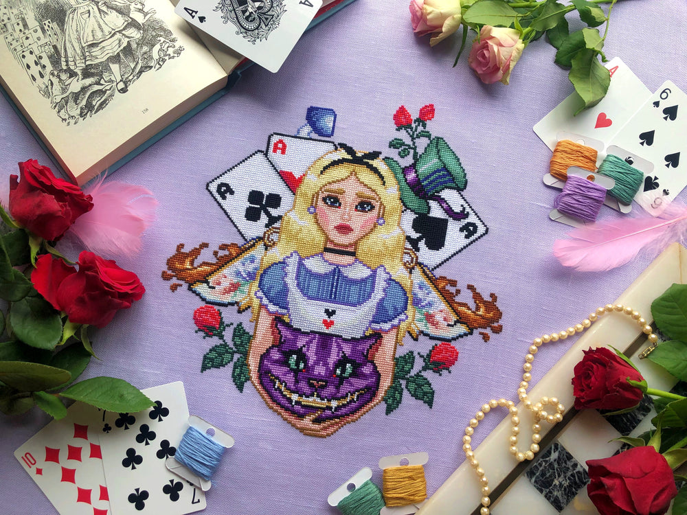 Alice in Wonderland cross stitch pattern front view. Piece is large and detailed. Alice is in the middle of the composition, holding the head of the Cheshire Cat in her arms. Alices hair is blonde with a black ribbon, her dress is blue and white.