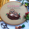 Front view of Nest Friends Forever owls cross stitch pattern. Two owls are nestled together in a nest made of branches and berries. There is one small owl and one big owl. Above them is the quote Nest Friends Forever. The birds are brown and cute.