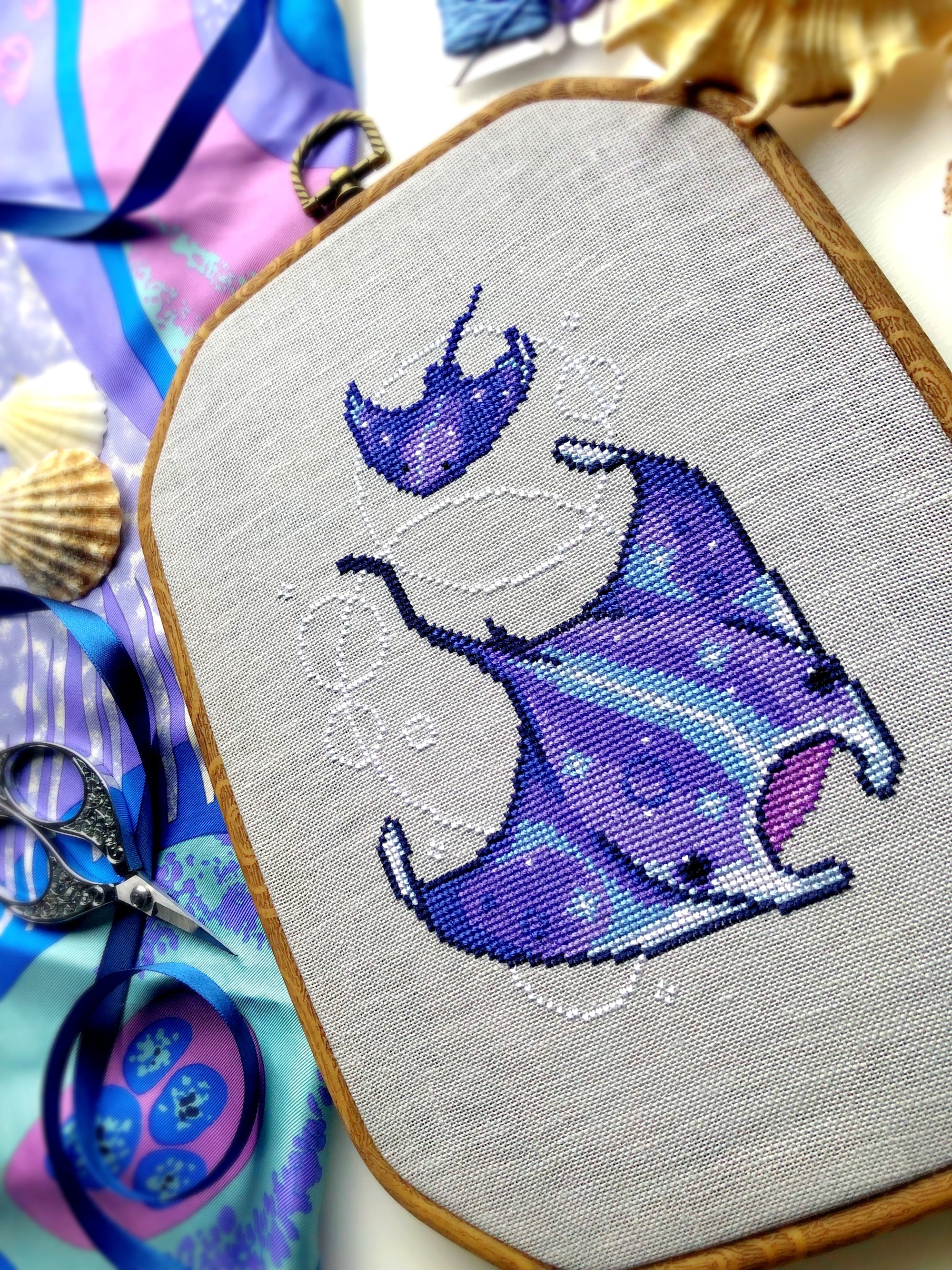 Slight closeup and angled view of ocean rays cross stitch pattern. Cross stitch pattern is of small to medium size. White bubbles are minimalist. Colors are vibrant and beautiful. Rays are soaring through the water.