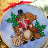 Angled front view of squirrel Nutracker cross stitch pattern. Colors are primarily blue, green, brown, red, purple, yellow and black. There are lots of details in all the elements. Squirrel looks realistic. He has a big tail and wears no pants.