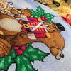 Closeup of squirrel cross stitch pattern, bottom righthand side. Stitches are neat and tidy. The pattern is rather large. Colors are vibrant and saturated. Especially the greens in the holly pop.