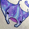 Closeup of manta ray, bottom right corner. Stitches are neat and tidy. Ray has a lighter middle back strip of light blue, whereas his flaps are mostly deep purple. The inside of his mouth is a dark, muted pink.