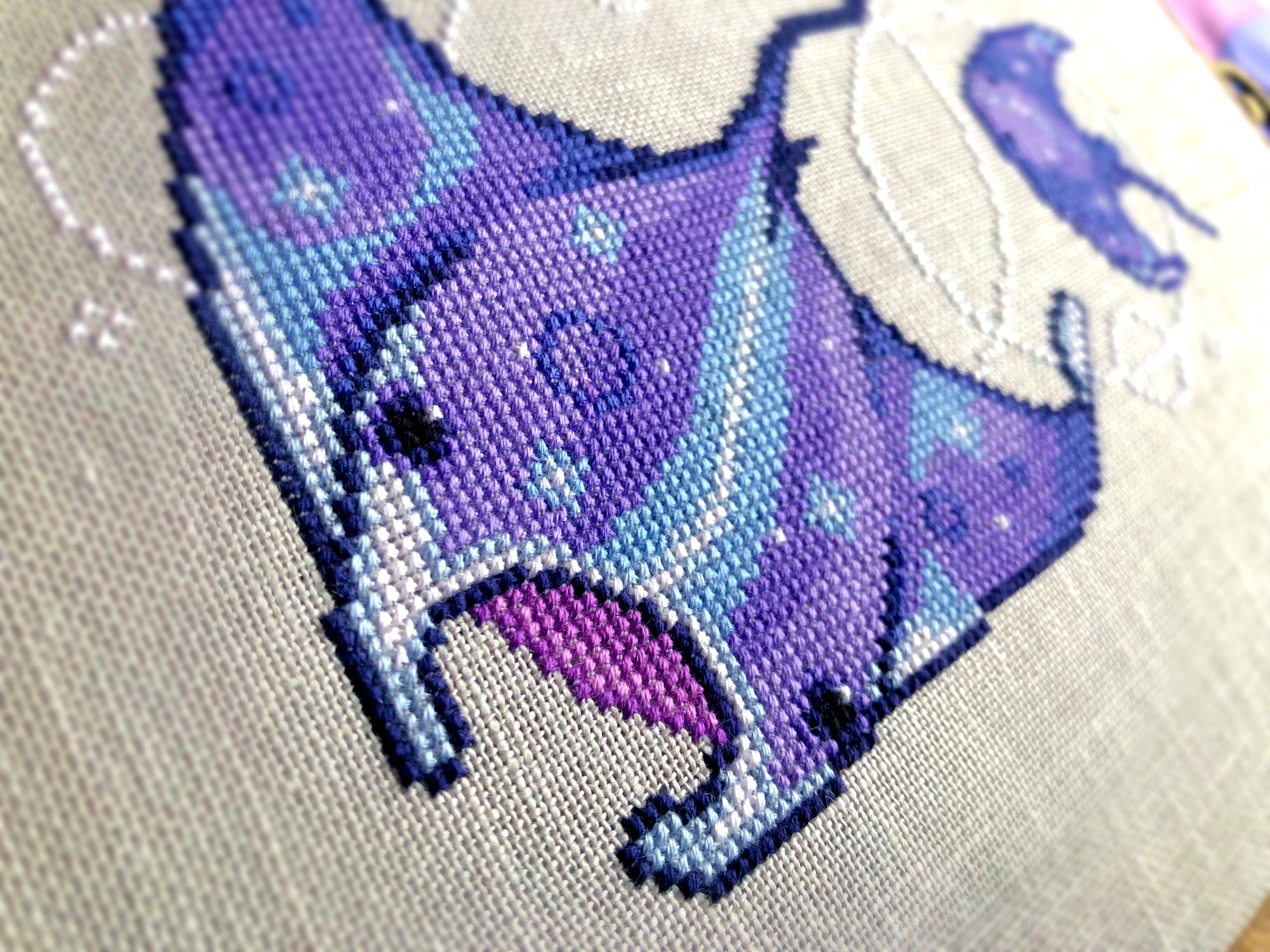 Closeup of manta ray, bottom right corner. Stitches are neat and tidy. Ray has a lighter middle back strip of light blue, whereas his flaps are mostly deep purple. The inside of his mouth is a dark, muted pink.