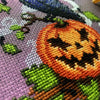 Closeup of Jack-Crow-Lantern design, lower left side. Here, the pumpkin and its grin are displayed. The halfstitch backstitch that forms the smoke is also clearly visible. Colors pop. Stitches are neat and fluffy. Lots of detail is visible.