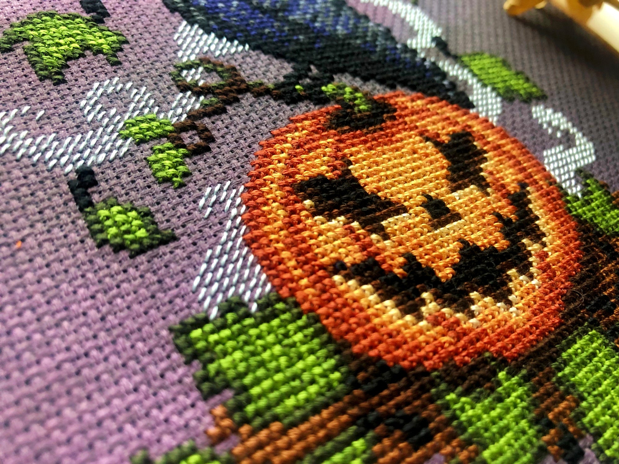 Closeup of Jack-Crow-Lantern design, lower left side. Here, the pumpkin and its grin are displayed. The halfstitch backstitch that forms the smoke is also clearly visible. Colors pop. Stitches are neat and fluffy. Lots of detail is visible.