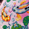 Closeup of Koi Fish cross stitch pattern. Right side is most visible. Finished piece is of medium size. There are two fish, surrounded by lotus leaves and flowers. The fish on the left is orange, the fish on the right is blue. Both have spots.