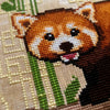 Closeup of Red Panda cross stitch pattern. The red pandas face is cute and round, and the scene is brightly colored. The details of the Chinese-inspired background are clearly visible. Bamboo shoots are placed behind the red pandas head and ears.