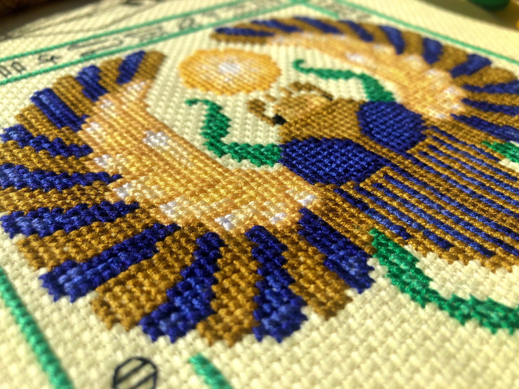 Closeup of Egyptian scarab cross stitch pattern. Angled view of the bottom left. Stitches are tidy. Colors are bright and beautiful.