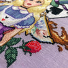 Closeup of righthand bottom side of Alice in Wonderland cross stitch pattern. One of the roses and teacups are particularly visible here. The teacup is a traditional English teacup, which brown tea is spilling out of. The rose is red and pink.