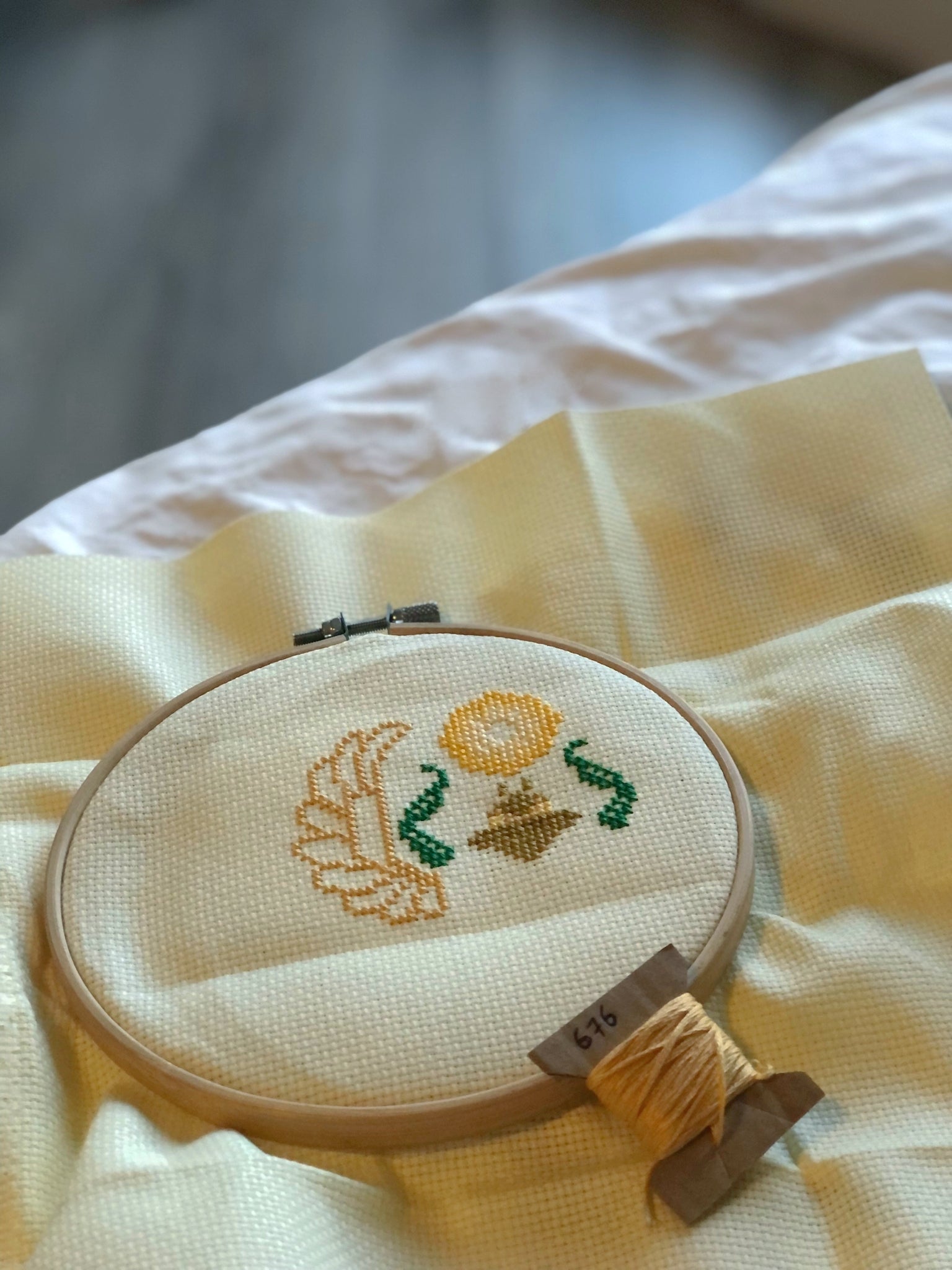 Picture of the work-in-progress of the Egyptian scarab cross stitch pattern. A small part of the pattern has been stitched: only the head, front paws, sun and part of the lefthand wing are visible. Piece is framed in a hoop, bobbin in the foreground.