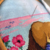 Work in progress on Platypus cross stitch pattern. Needle is visible and is stiching through the 16ct Aida fabric. The pink and blue sky with birds is being stitched. Stitches are fluffy and tidy. Danish stitching method is used. 
