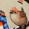 Closeup of Winter Birds cross stitch pattern. Image is zoomed in on the wren. He is very cute and round. The wren is wearing an orange, striped hat with pompoms, and looks very warm. The colors of his feathers are brown and white.