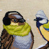 Closeup of Winter Birds cross stitch pattern. Image is zoomed in on the sparrow. He is a very cute bird that also looks very hip. The bird is wearing a green scarf and earmuffs, and looks very warm. The colors of his feathers are brown, beige, grey.